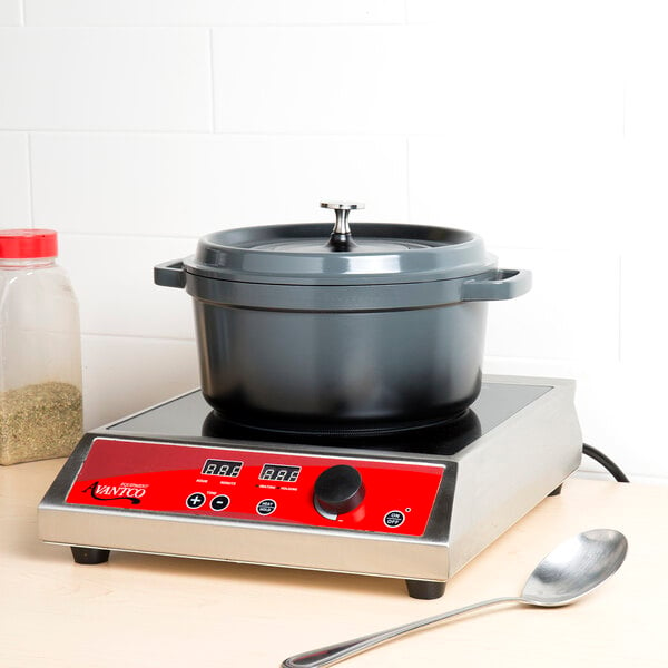 A GET gray enamel coated cast aluminum Dutch oven with lid on a red stove with a spoon.