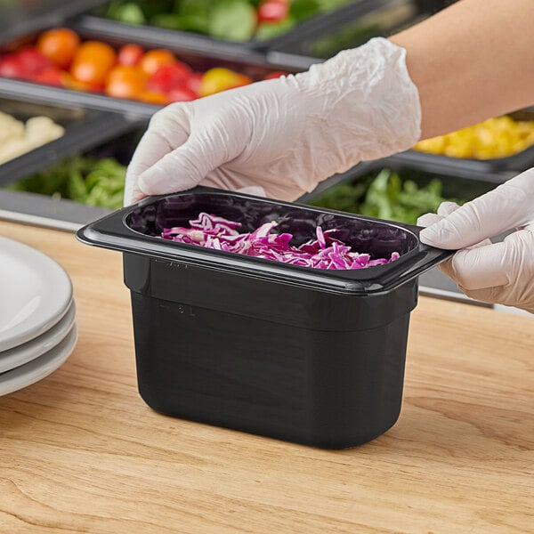A person in gloves holding a black Cambro food container filled with shredded cabbage.