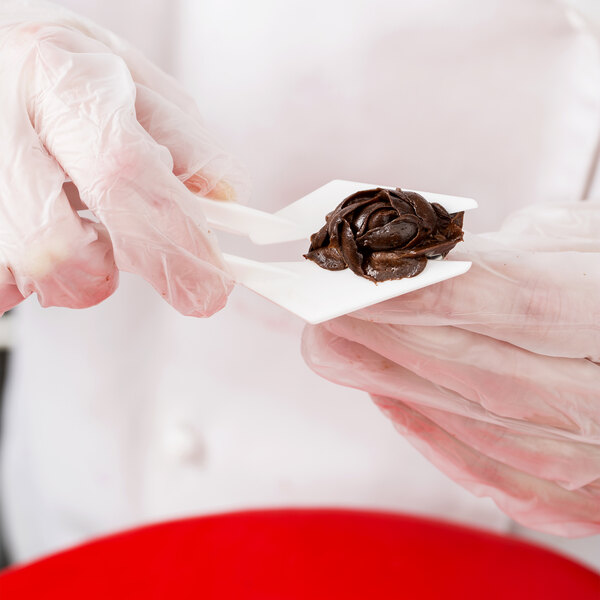 A person using a white Ateco plastic flower lifter to decorate a piece of food.