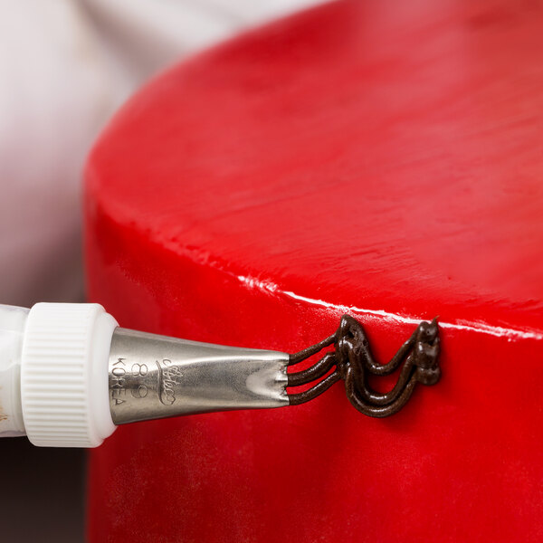 A person using an Ateco 3-hole piping tip on a pastry bag to pipe red cake.