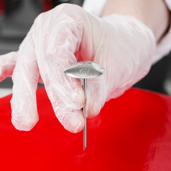 A person holding a Ateco stainless steel flower nail.