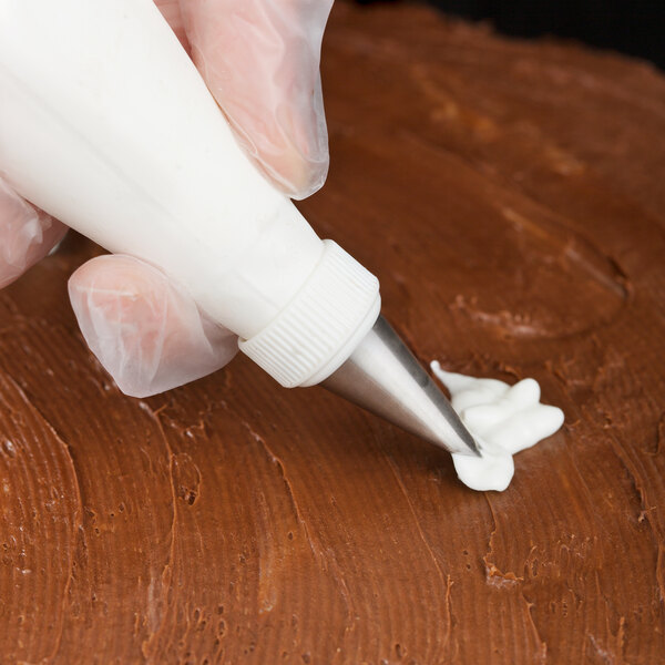 A person using an Ateco leaf piping tip to decorate a cake with a pastry bag.