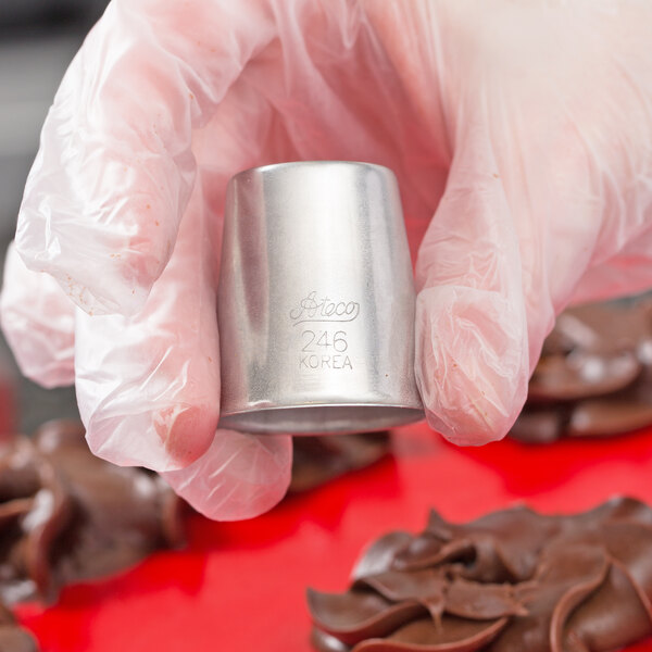 A hand in a glove holding a silver Ateco Russian piping tip.
