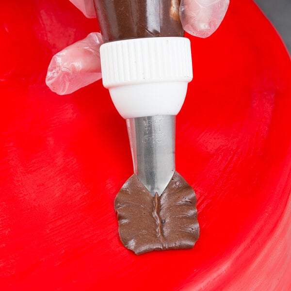 A hand holding an Ateco leaf piping tip over a brown substance in a pastry bag.