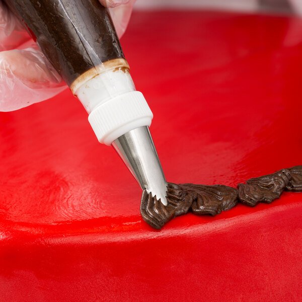 A person using an Ateco leaf piping tip to decorate a red cake.