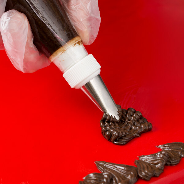 A hand using an Ateco leaf piping tip with a pastry bag over a red surface.