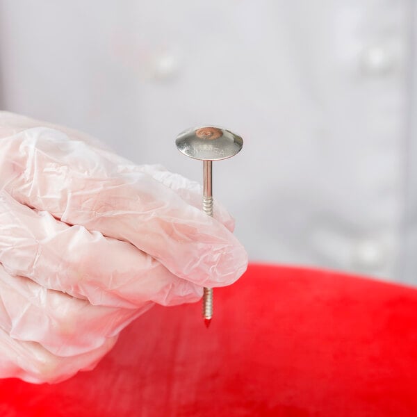 A hand in gloves holding an Ateco stainless steel flower nail.