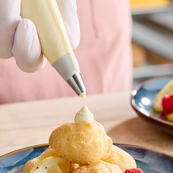A hand using an Ateco plain piping tip on a plate of food.