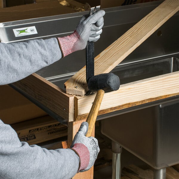 A person wearing a Cordova Machinist cut resistant glove with gray palm coating using a hammer to nail a piece of wood.