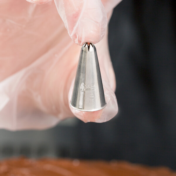 A hand holding an Ateco pastry bag with a cross-top piping tip.