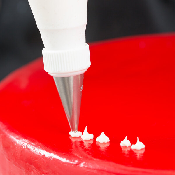 White plastic Ateco Cross-Top Piping Tip being used with a pastry bag to pipe icing on a cake.