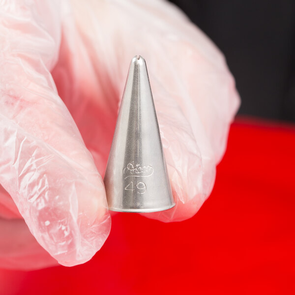 A hand holding a silver cone-shaped metal piping tip.
