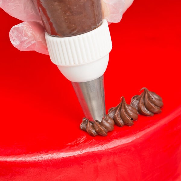 A hand using an Ateco Drop Flower piping tip on a red cake.