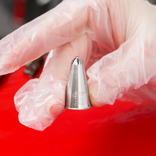 A hand holding a metal Ateco 129 drop flower piping tip.