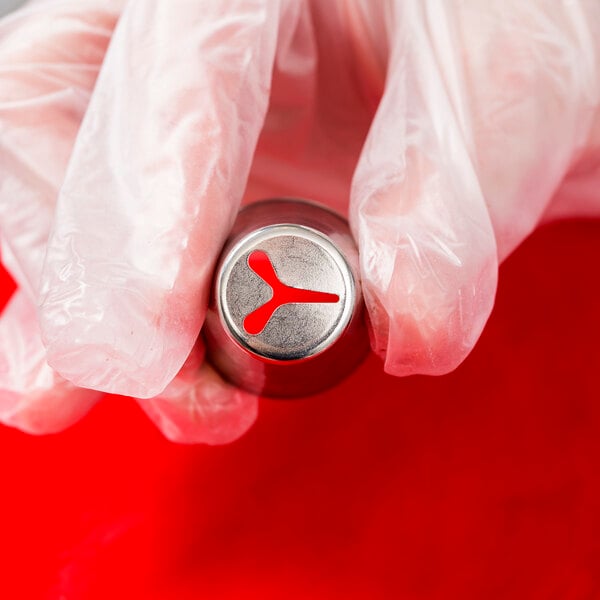 A hand holding a silver Ateco piping tip with a red logo.
