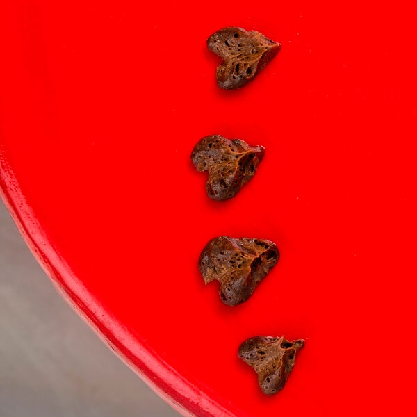 Brown hearts piped onto a red surface with the Ateco 252 Heart piping tip.