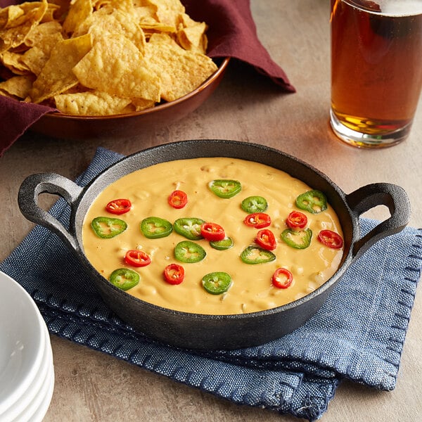 A Valor pre-seasoned cast iron round casserole dish filled with food next to a bowl of tortilla chips.