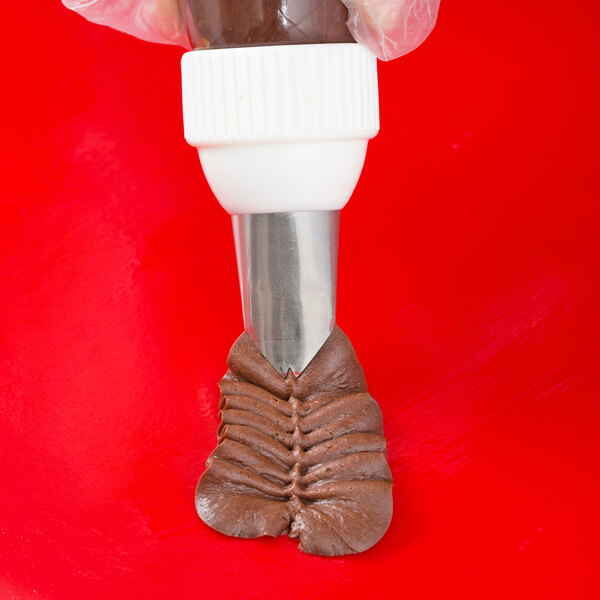 A hand holding a pastry bag with a leaf piping tip and brown frosting.