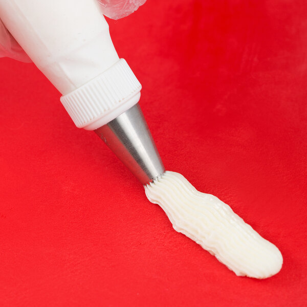A person using an Ateco drop flower piping tip to pipe white frosting.