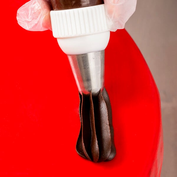 A hand holding a pastry bag with a swirled chocolate cake.