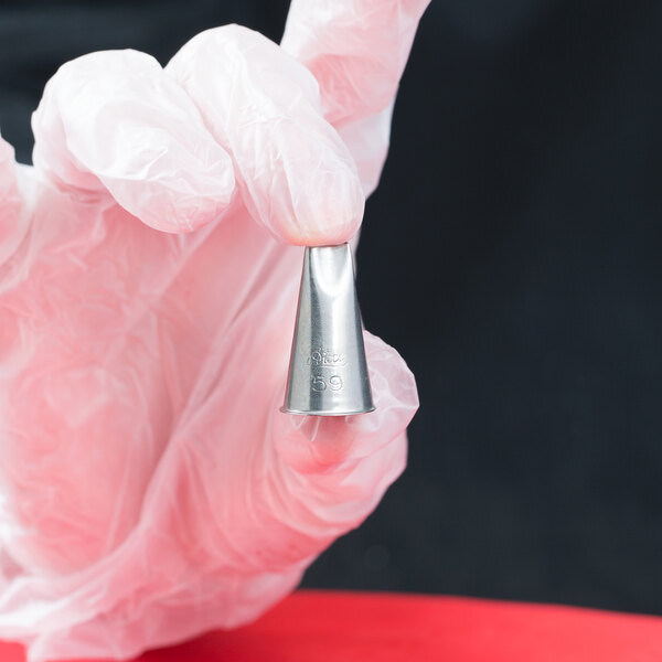 A hand in a glove holding an Ateco curved petal piping tip.