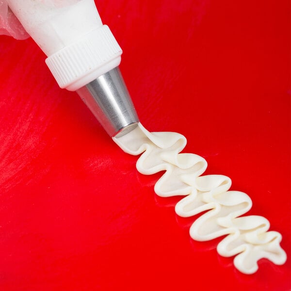 A person using an Ateco U-shape ruffle piping tip to pipe white frosting in a swirl.