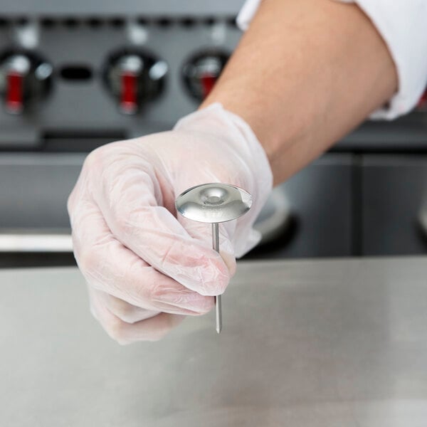 A person's gloved hand holding an Ateco stainless steel flower nail.