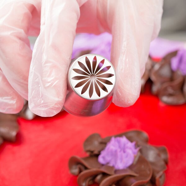 A hand holding a metal Ateco Russian piping tip with a flower design.