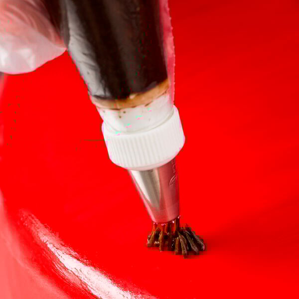 A pastry bag with grass-shaped frosting on a red surface.
