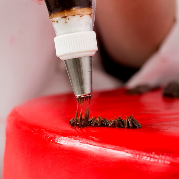 A person using an Ateco grass piping tip to decorate a cake with a pastry bag.