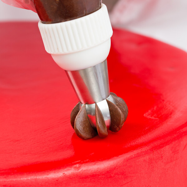 A person using an Ateco Russian ball tip to pipe red frosting on a cupcake.