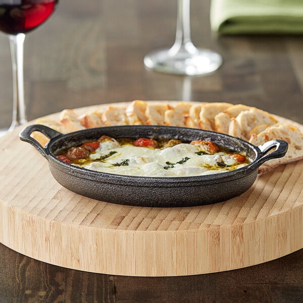 A Valor mini cast iron casserole dish filled with cheese and sauce on a table in a restaurant.