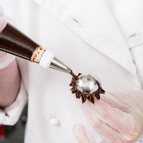 A person in white gloves using an Ateco domed flower nail to decorate a pastry.