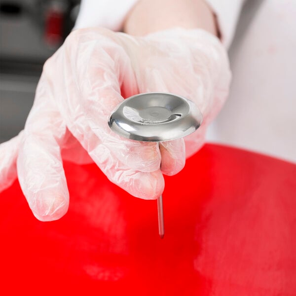 A person holding a stainless steel Ateco flower nail.