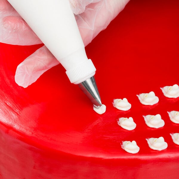 A hand using an Ateco curved petal piping tip to decorate a red cake.
