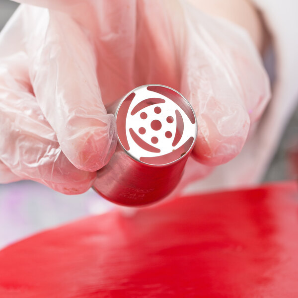 A person in gloves using an Ateco Russian piping tip on a red surface.