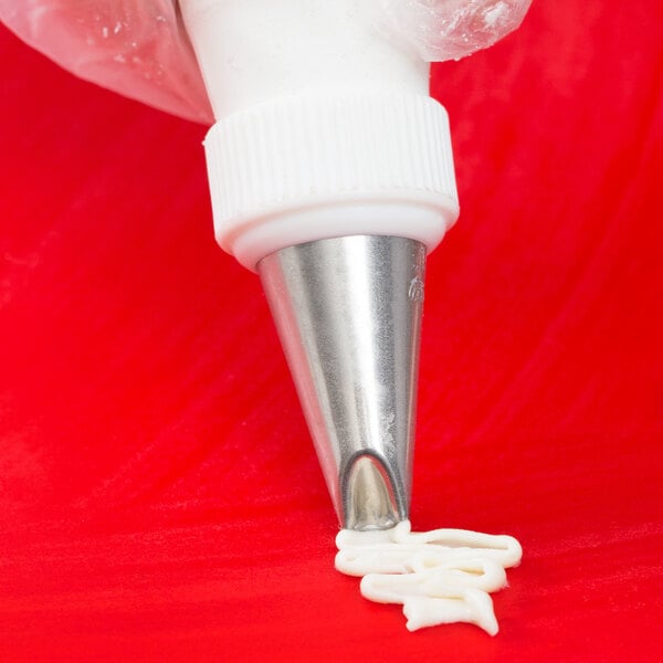 A pastry bag with a white Ateco Lily-of-the-Valley piping tip being used to pipe white frosting.