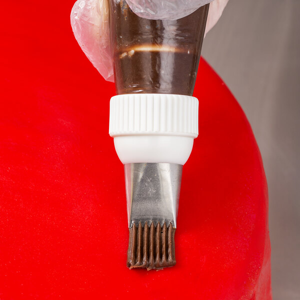 A hand using an Ateco basketweave piping tip to pipe chocolate icing onto a cake.