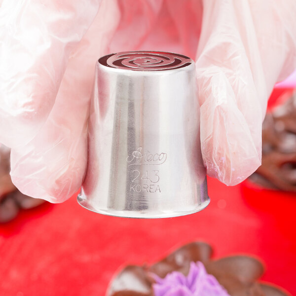 A hand holding a silver metal Ateco Russian piping tip with a swirl design.