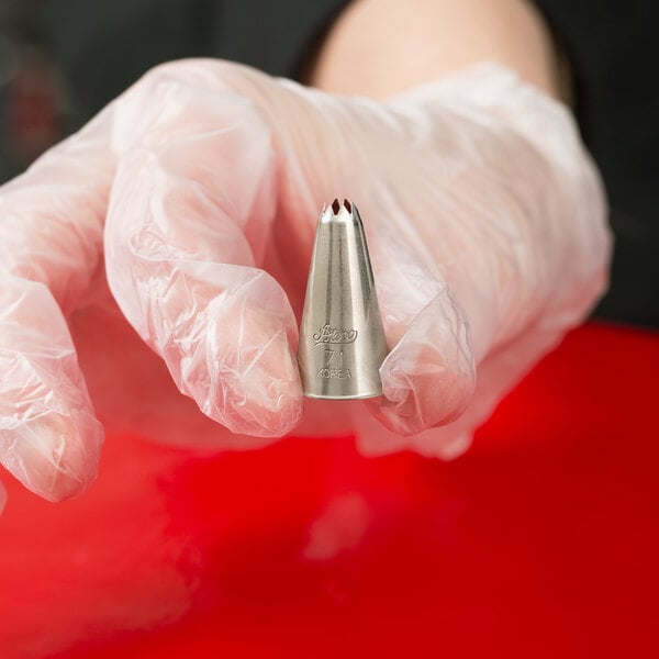 A hand in a plastic glove holding an Ateco leaf piping tip.