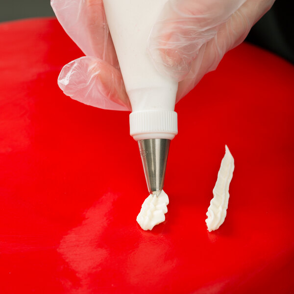 A hand using an Ateco leaf piping tip with a pastry bag to decorate a cake.