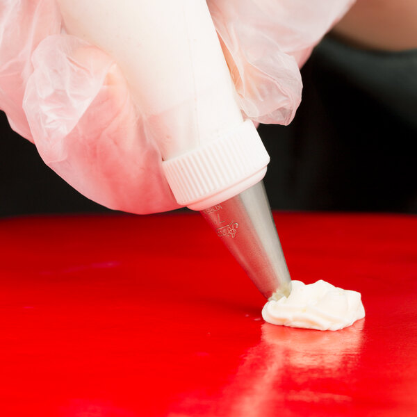 A hand using an Ateco leaf piping tip with a white frosting bag over a red surface.