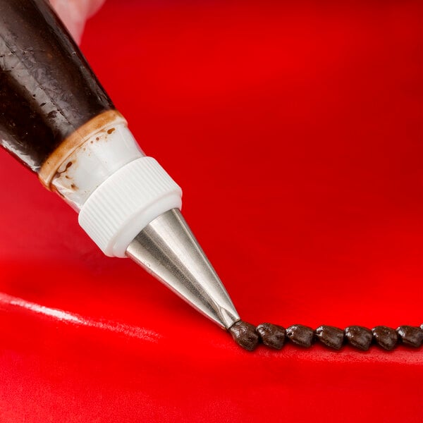 A person using an Ateco square tip on a pastry bag to pipe a brown line.
