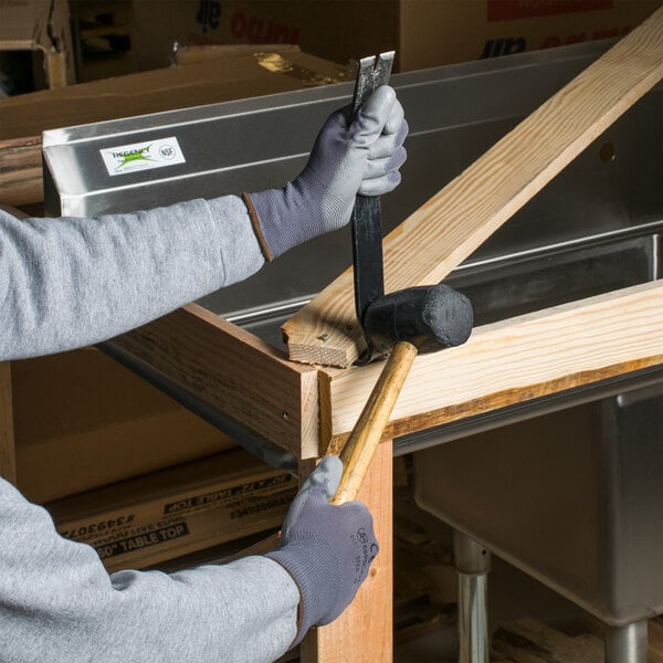 A person wearing Cordova gray warehouse gloves with gray palm coating using a hammer.