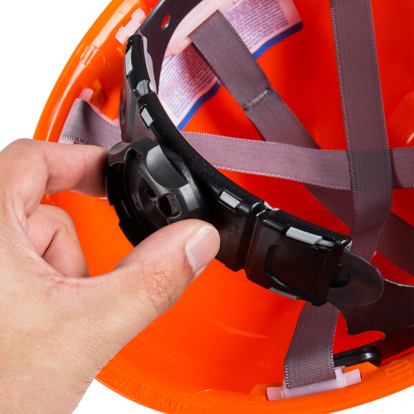 A hand holding a Cordova orange safety helmet with a black strap.