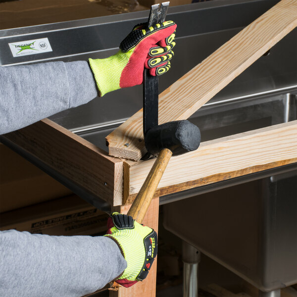 A person wearing Cordova yellow and red cut resistant work gloves using a hammer and mallet to fix a wooden table.