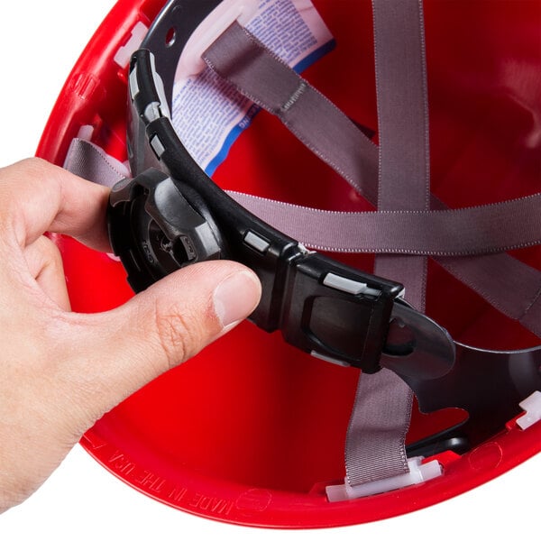 A person holding a red Cordova Duo Safety hard hat with a strap.
