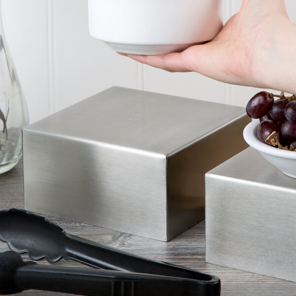 A hand holding a stainless steel square bowl filled with grapes.