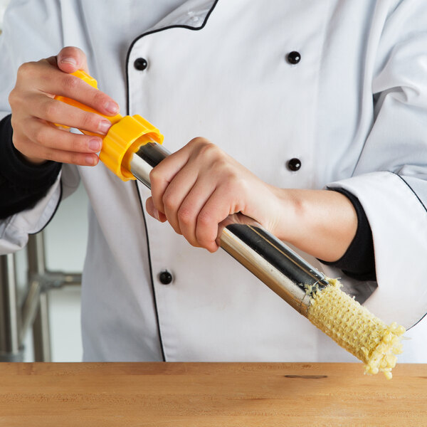 A person using a Weston corn stripper to peel corn on a table.