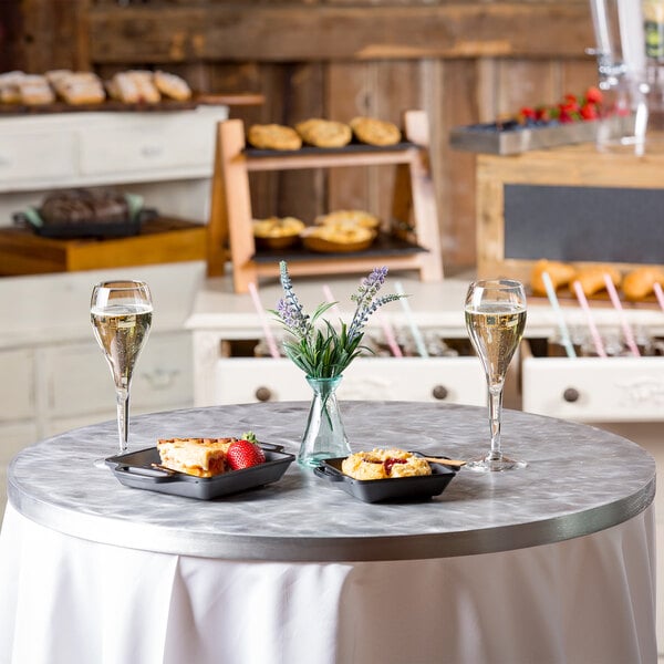 A Tablecraft round aluminum table cover with random swirl design on a round table set with food and wine.